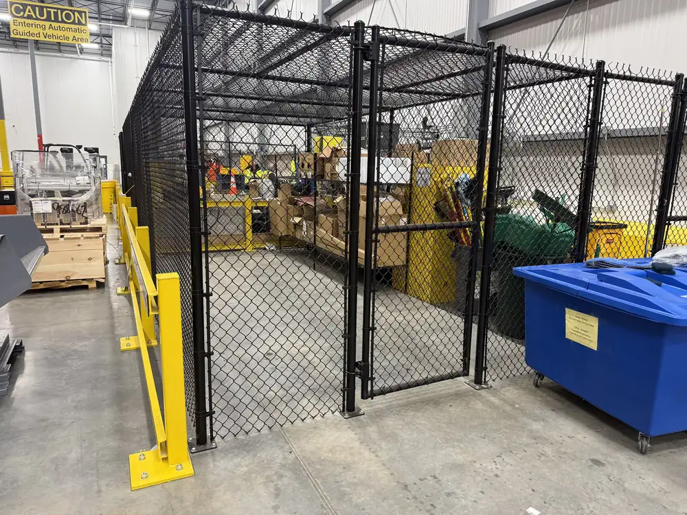 Black chain link security cage with a gate, inside a plant